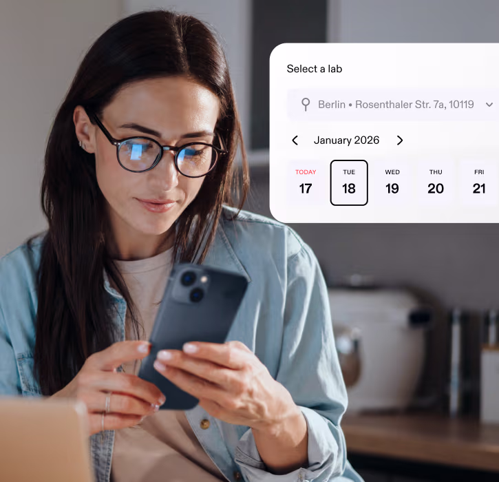 Woman with glasses looking at her smartphone with a lab selection and calendar interface overlay showing dates in January 2026 for Berlin location.
