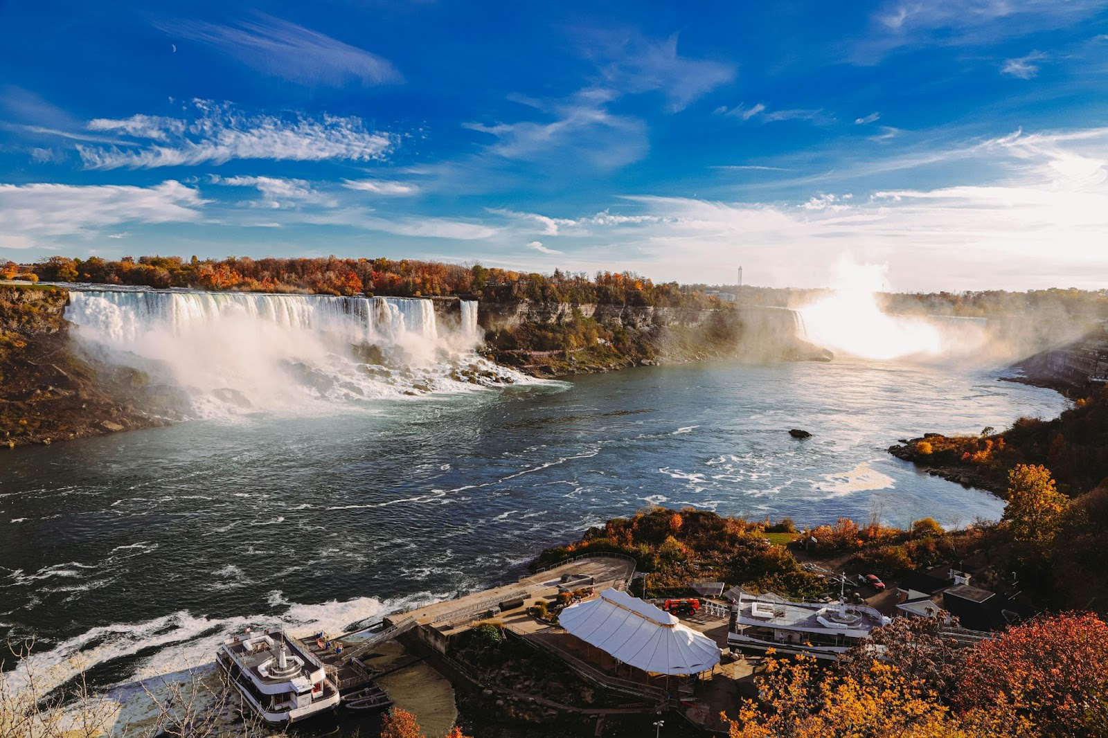 Stunning view of Niagara Falls near Toronto, with mist rising and vibrant fall colors under a bright blue sky.