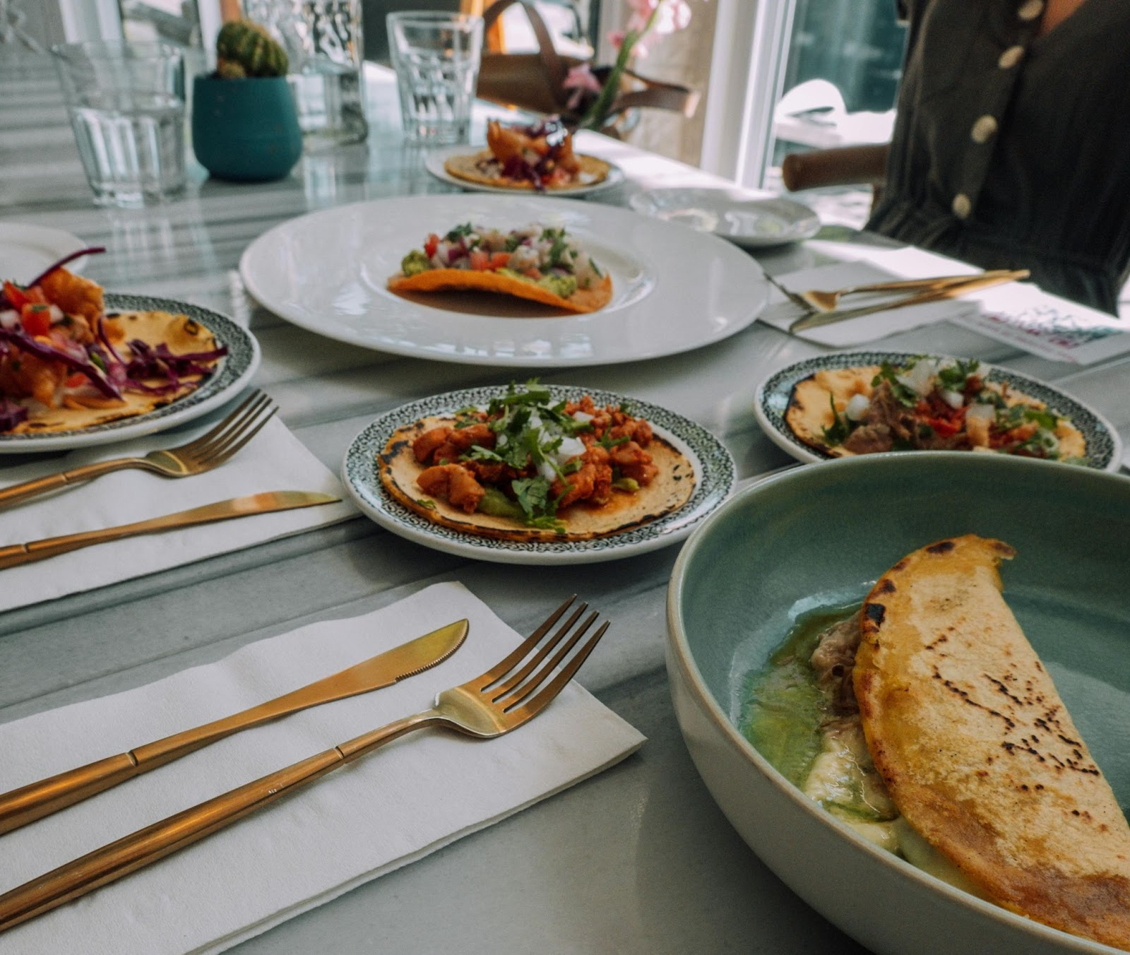 A cozy Toronto restaurant table set with gourmet tacos, tostadas, and gold cutlery under natural light.