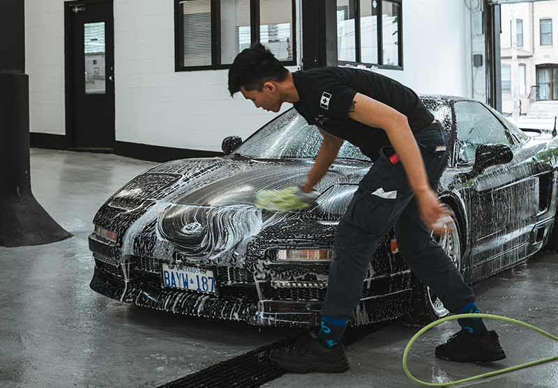 A car detailing technician washing a black sports car covered in foam at a professional car detailing Toronto shop. Example of best car detailing Toronto with attention to detail and premium cleaning techniques for high-end vehicles.