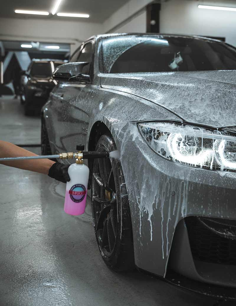 Close-up of a gray luxury car receiving foam application during Toronto auto detailing service. The process highlights thorough car cleaning Toronto and care used by expert technicians at a premium car detailing service.