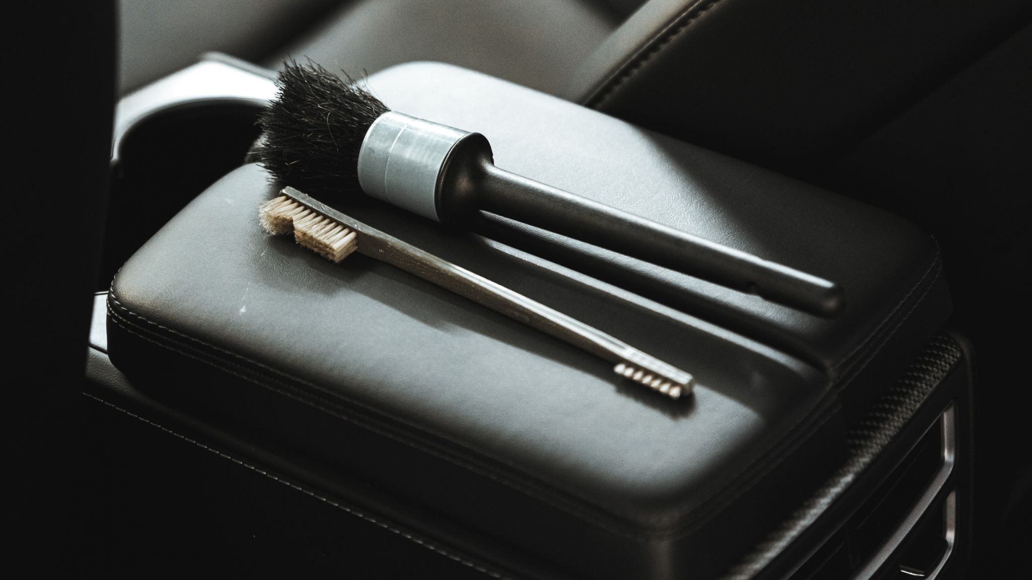 Detailing brushes placed neatly on a leather car armrest inside a luxury vehicle, ready for interior cleaning during an Alphashine car detailing service in Toronto.