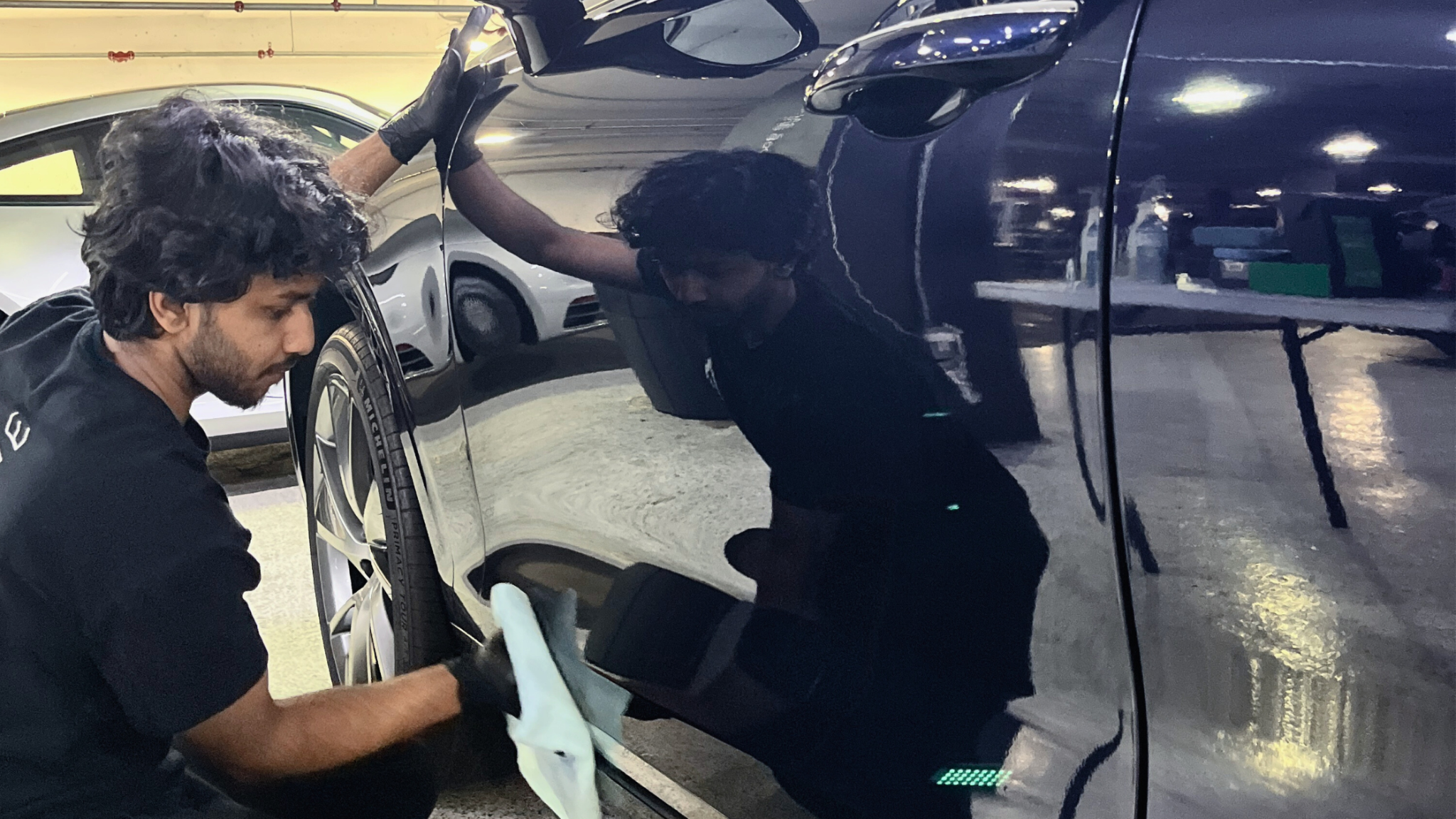 An ALPHASHINE detailer carefully wiping the side of a dark luxury vehicle during a ceramic coating service in Toronto, with a deep mirror like reflection showing the quality of the finish.