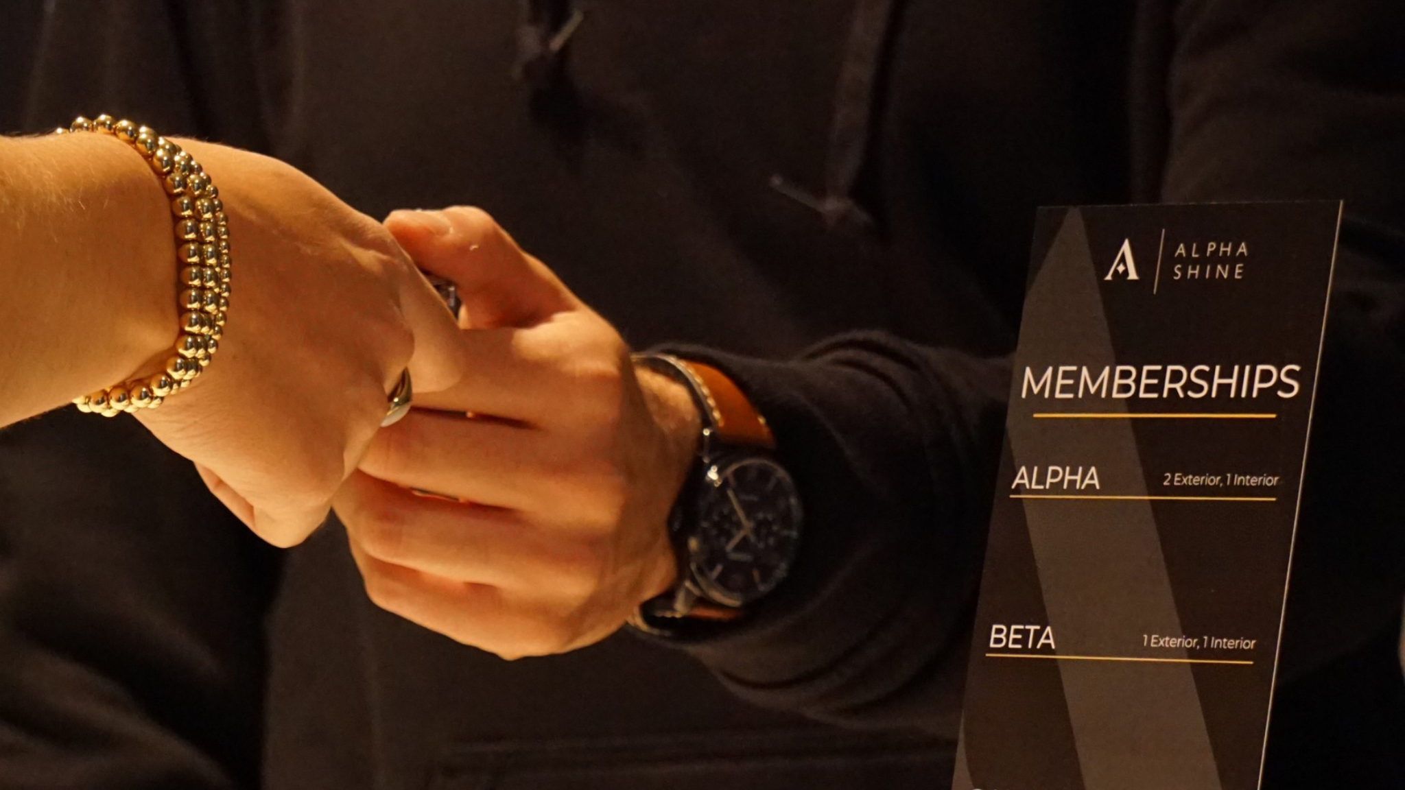 A customer receiving an ALPHASHINE membership card at the front desk, with a display showing membership options and a focus on premium car care services.