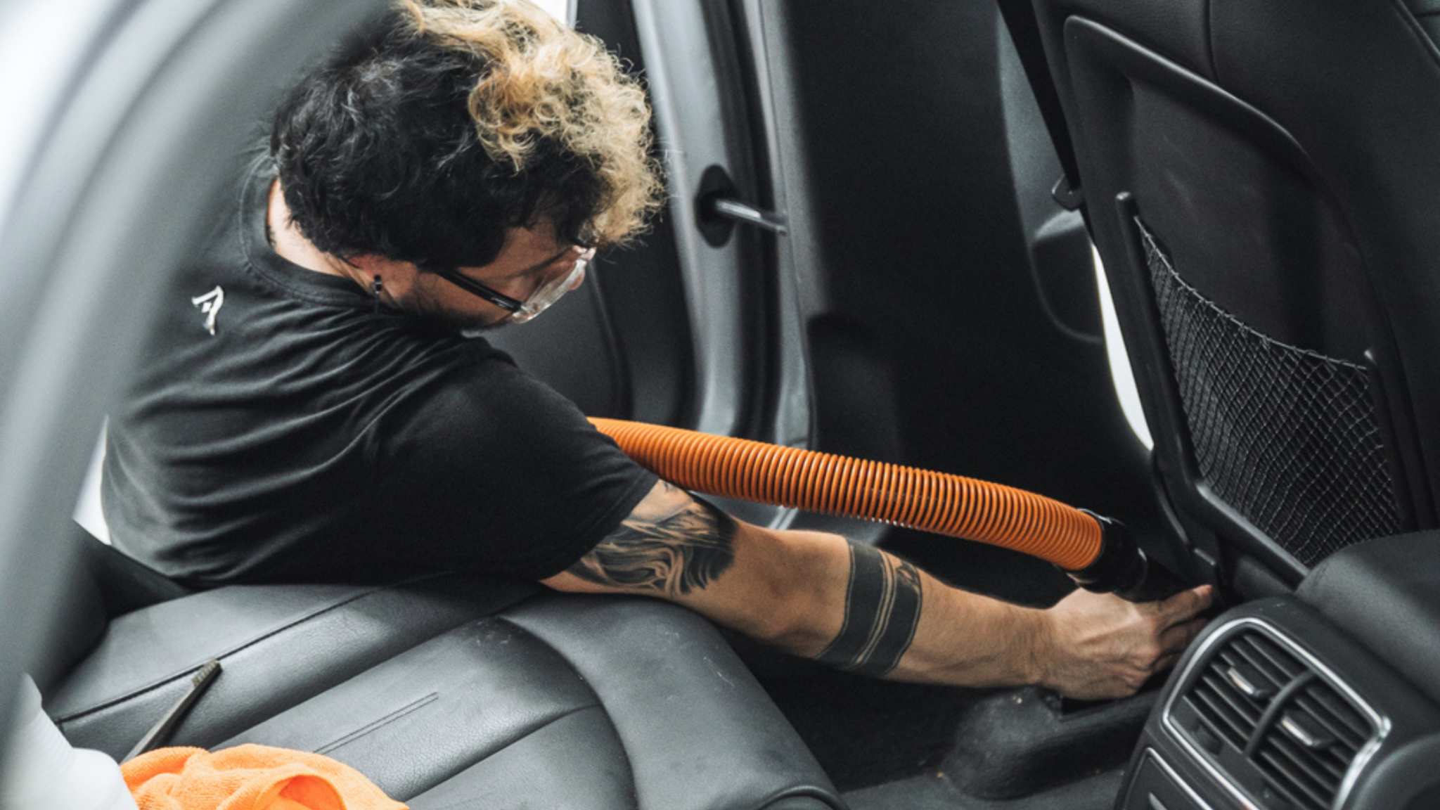 Professional ALPHASHINE car detailer vacuuming rear seat area during interior car detailing service, removing dirt and debris from hard to reach areas.