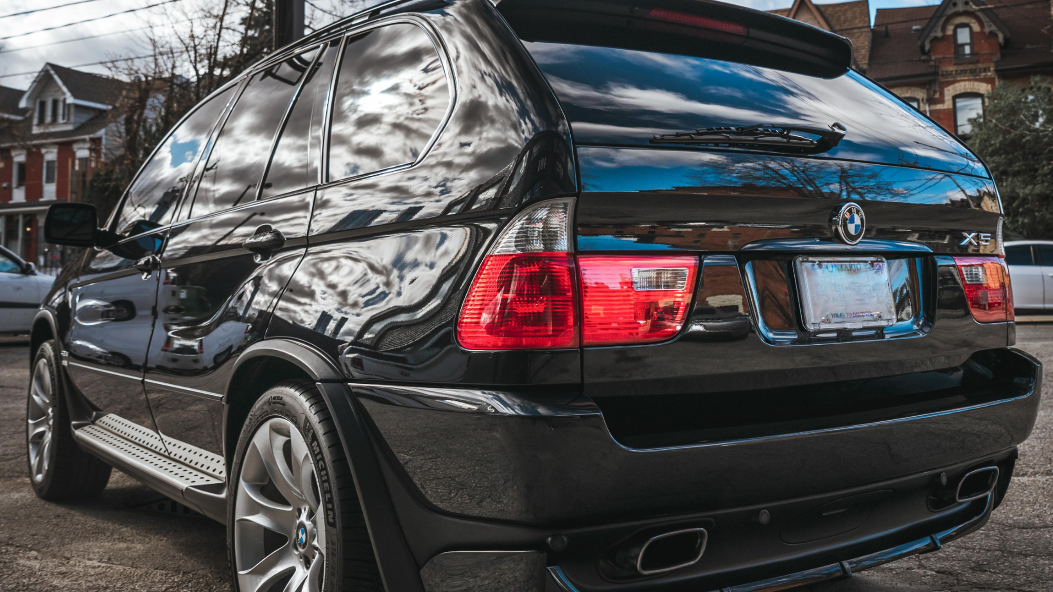 Clean black BMW SUV exterior after professional car detailing, showing glossy paint finish and clear reflections on the rear and side panels.