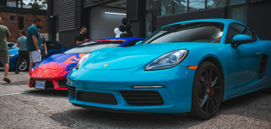 Bright blue Porsche sports car parked alongside other luxury vehicles at an outdoor event, showcasing a clean glossy finish from ALPHASHINE professional car detailing services near Lawrence Park in Toronto.