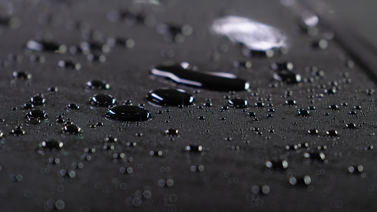 Close up of water droplets beading on a dark car surface, highlighting a smooth, glossy finish with shallow depth of field.