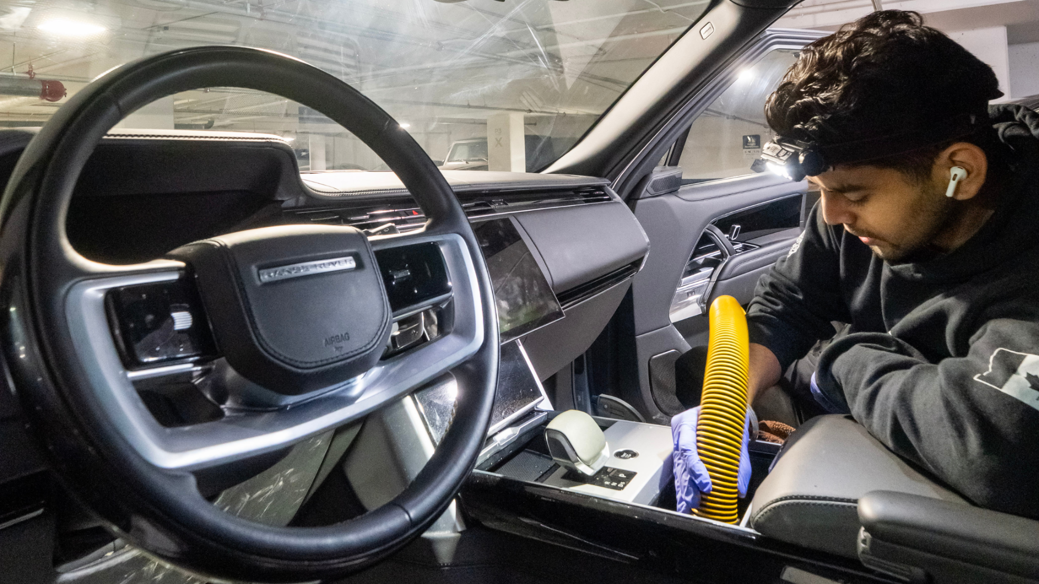 ALPHASHINE detailer cleaning rear floor area of a car interior with a vacuum and inspection light, targeting debris in carpeted surfaces.
