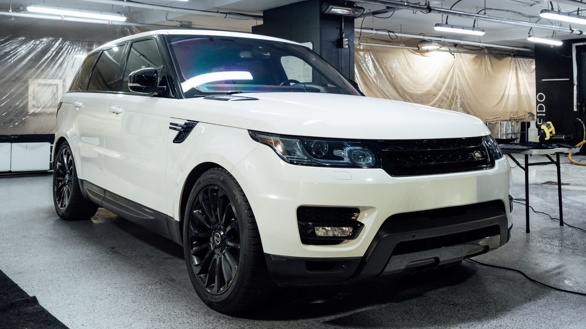 White Range Rover parked inside a detailing shop, freshly cleaned exterior under bright indoor lighting.