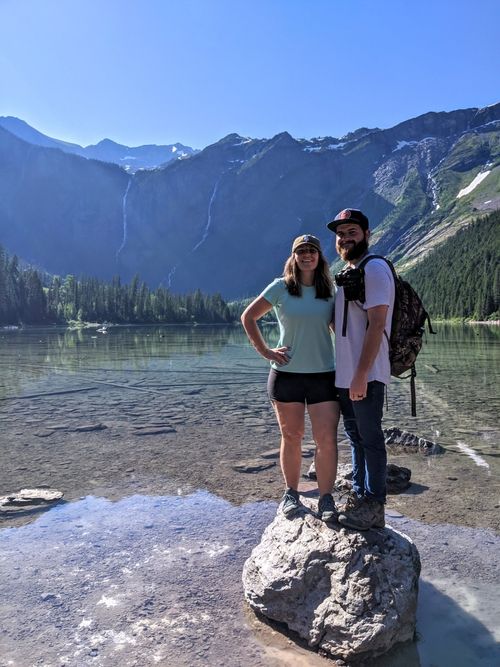 Two buffalo standing side by side in a golden field as the sun flares over a distant mountain top.