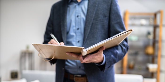 Man in a blazer writing notes on a clipboard during a seminar or meeting.