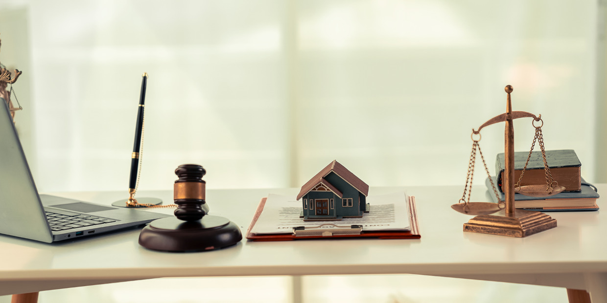 Real estate attorney desk with legal documents, house model, judge's gavel, scales of justice, and laptop symbolizing property law and legal services.