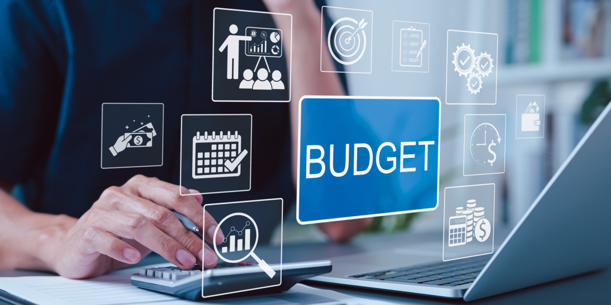 Person using a calculator and laptop with digital budgeting and financial icons displayed on screen.