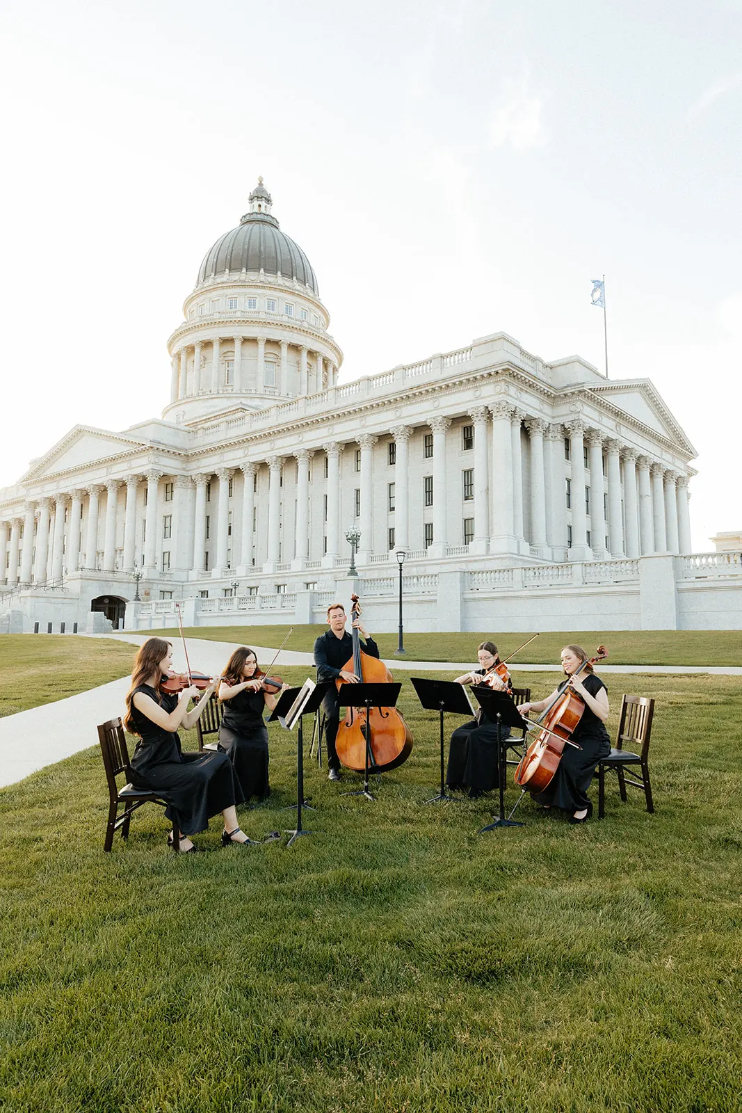 A photo of Artiva String Quartet laughing and holding their instruments by a lake.