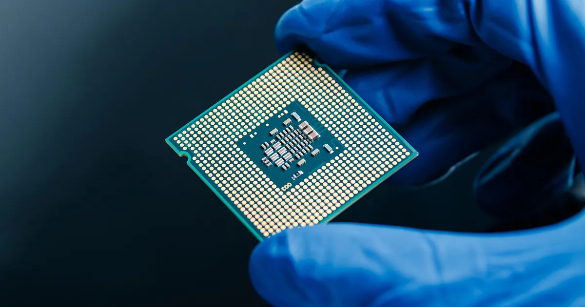 A hand holding a microchip with several transistors. 