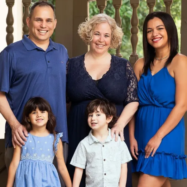 Smiling diverse family of five posed on porch with balusters, including two children and three adults