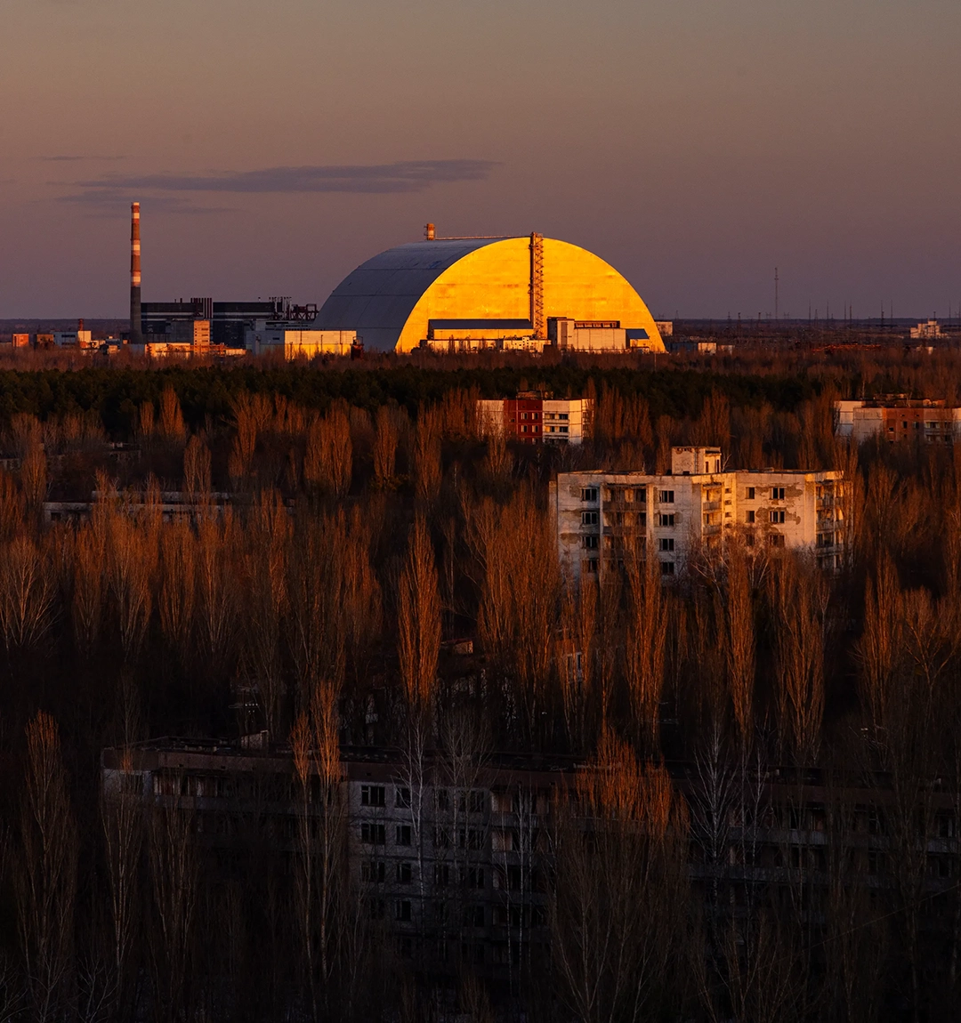 Housing blocks in Pripyat stand derelict near the 360ft-high dome of the New Safe Confinement. © Gerd Ludwig, 2026