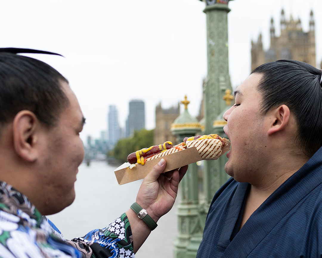 Hōshōryū Tomokatsu (left) feeds Ōnosato Daiki a hot dog near the Houses of Parliament during a tour of central London. Photograph: Ryan Pierse/Getty Images
