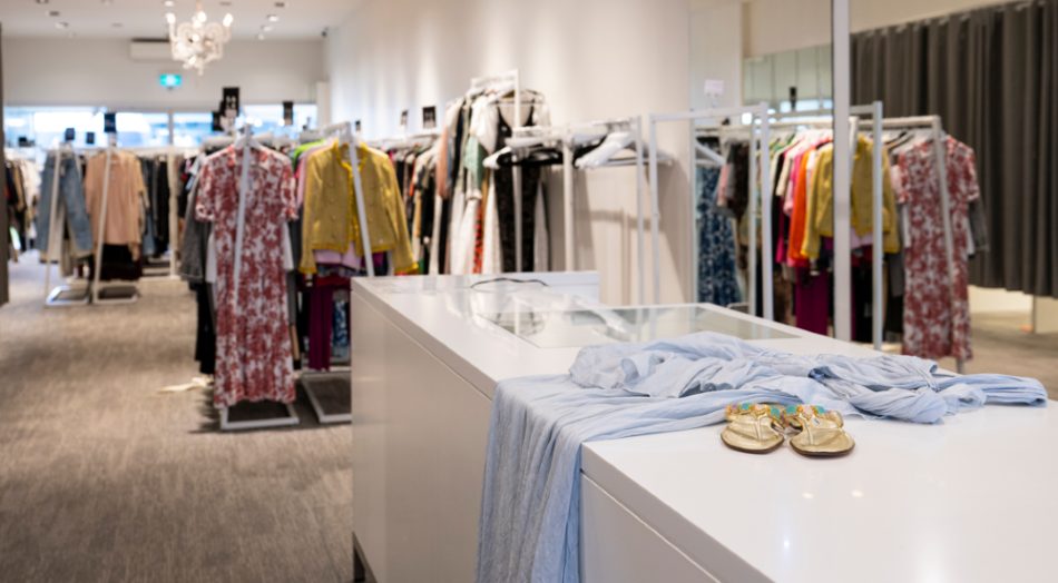 Racks of preloved designer fashion inside a VENLA store, with a blue dress and gold sandals on the counter