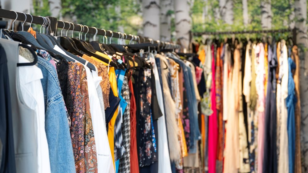 Racks of colourful preloved clothing at VENLA in front of a birch forest wall