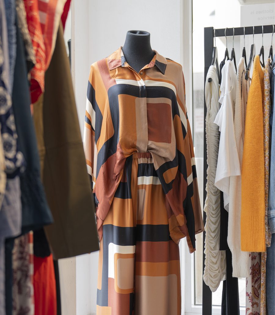 Mannequin in a printed satin shirt and trousers beside racks of preloved clothes at VENLA