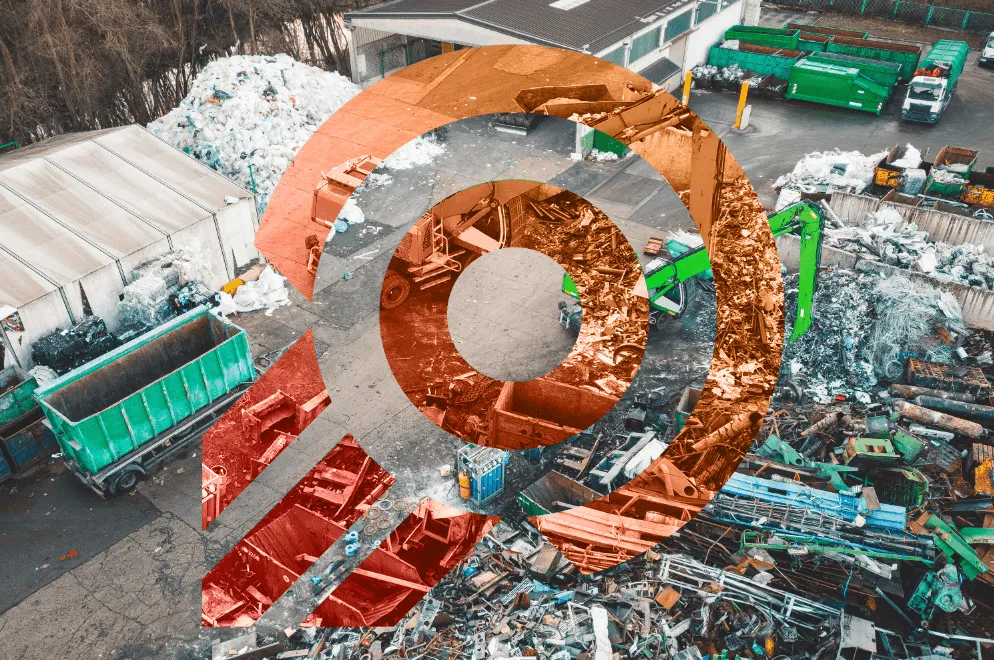 Aerial view of a recycling center with piles of metal scrap, green containers, and a green crane sorting waste.