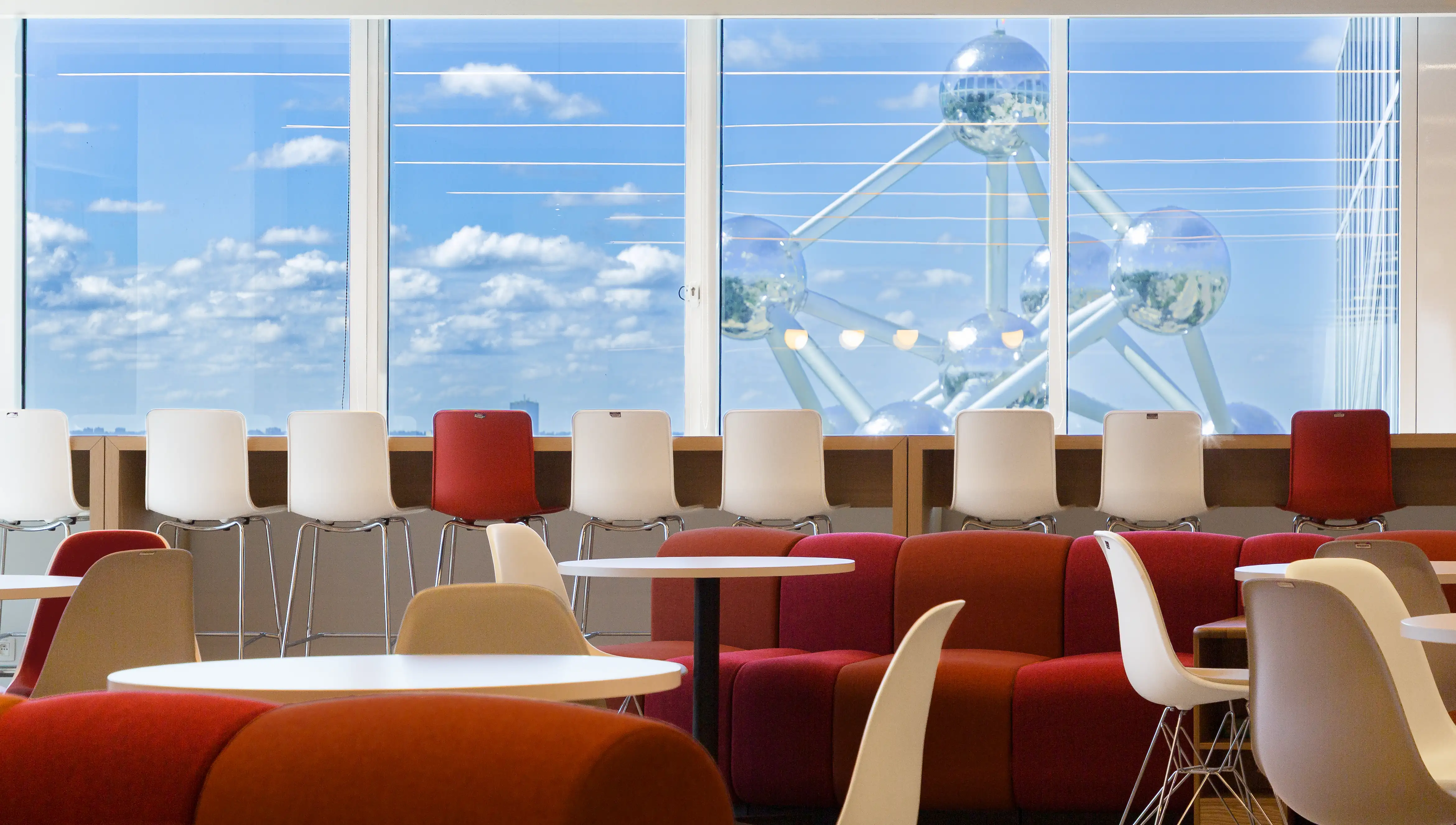 Espace communautaire avec un grand canapé coloré et des sièges donnant sur l'Atomium dans les bureaux bruxellois de Henkel, rénovés par Space Refinery.