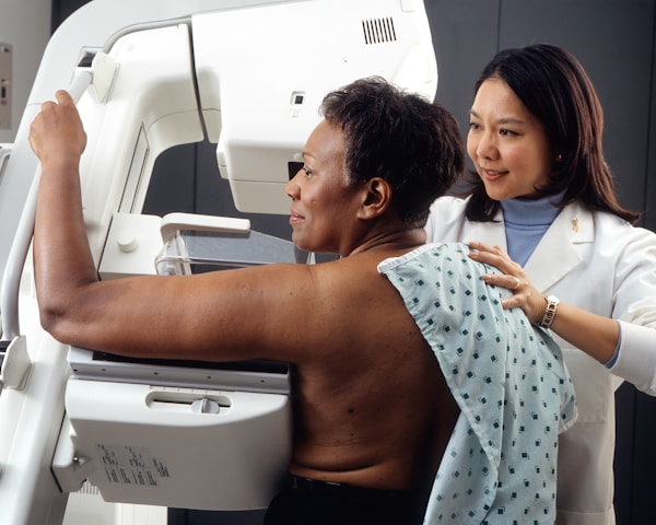 Woman Receives Mammogram.
An Asian female technician positions an African-American woman at an imaging machine to receive a mammogram.
Creator:	Rhoda Baer
