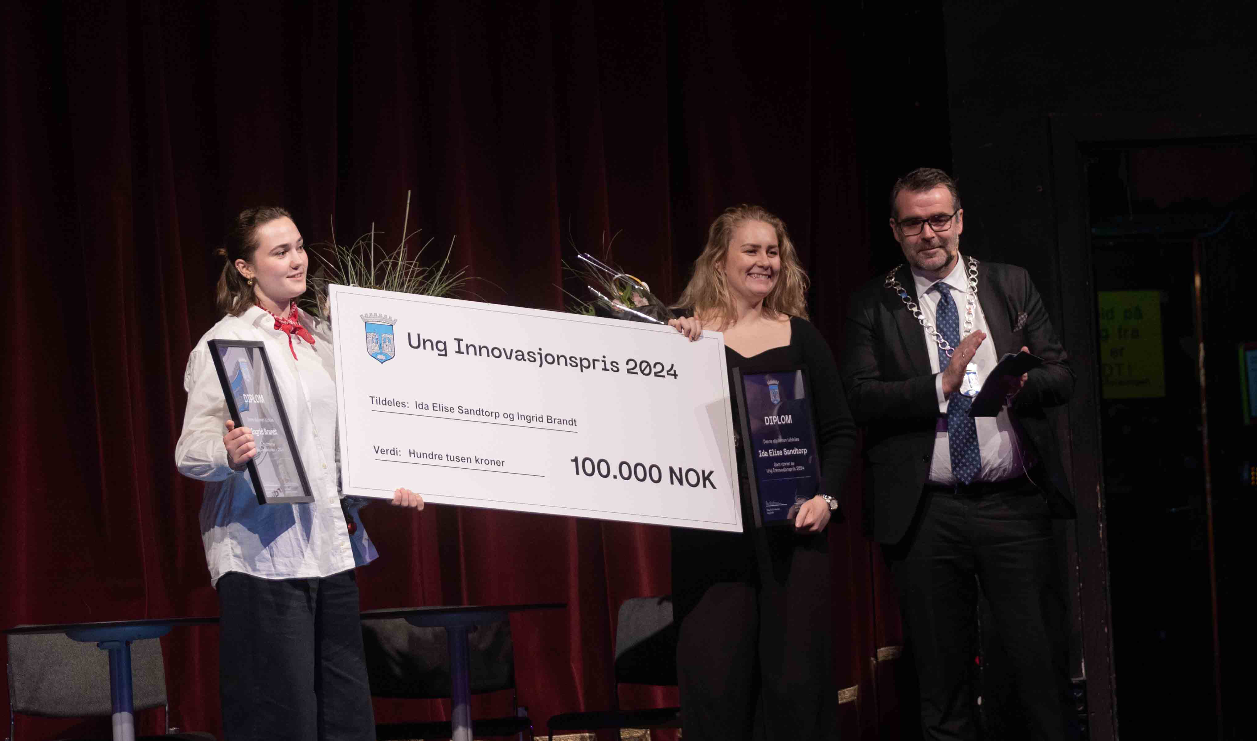 Fjorårets vinnere, Ida Elisa Sandtorp og Ingrid Brandt, tar imot prisen fra ordfører Kent Ranum, på scenen på Studentersamfundet. 