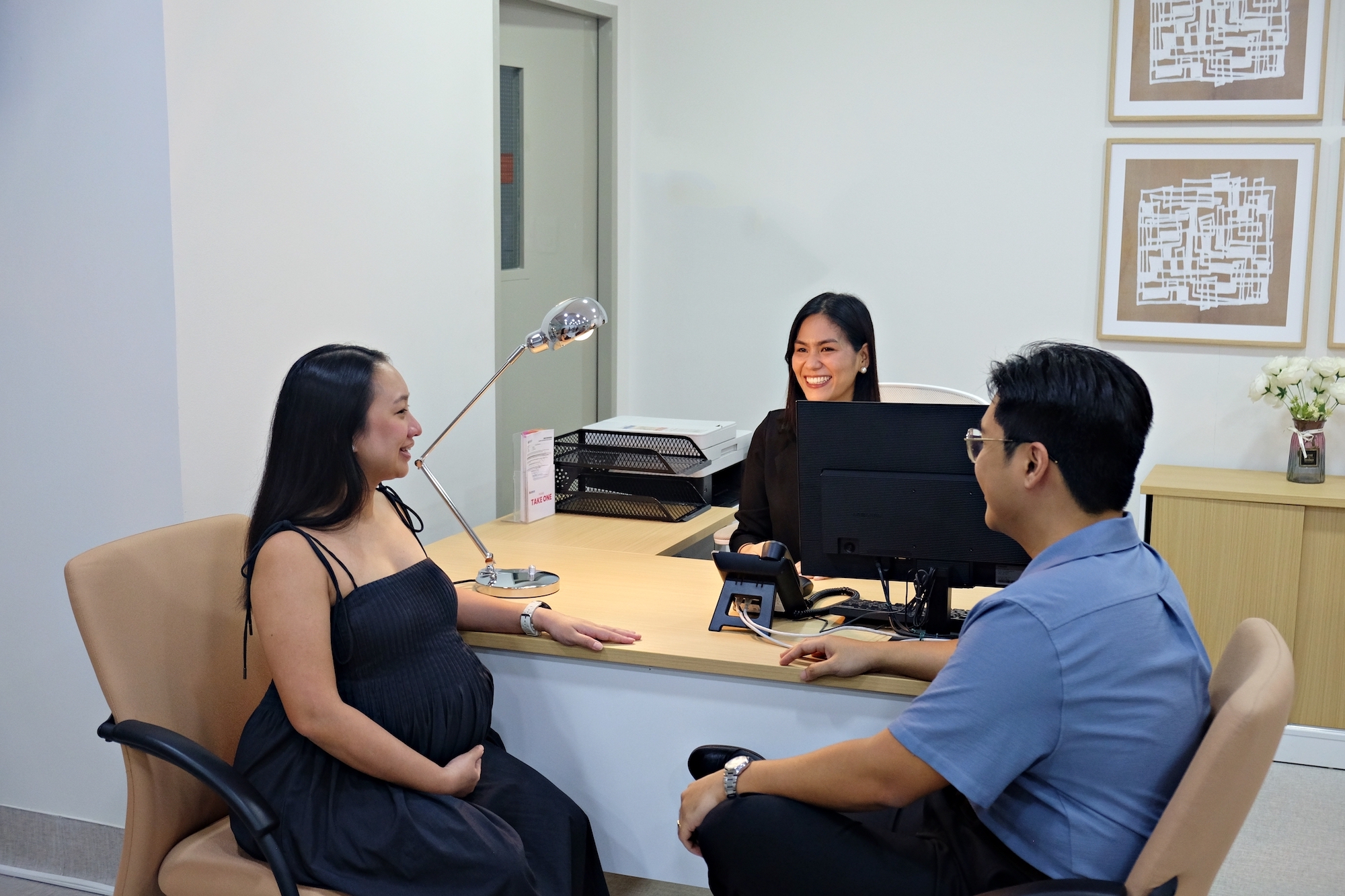 A pregnant woman and man at a reception desk in a hospital with an receptionist assisting