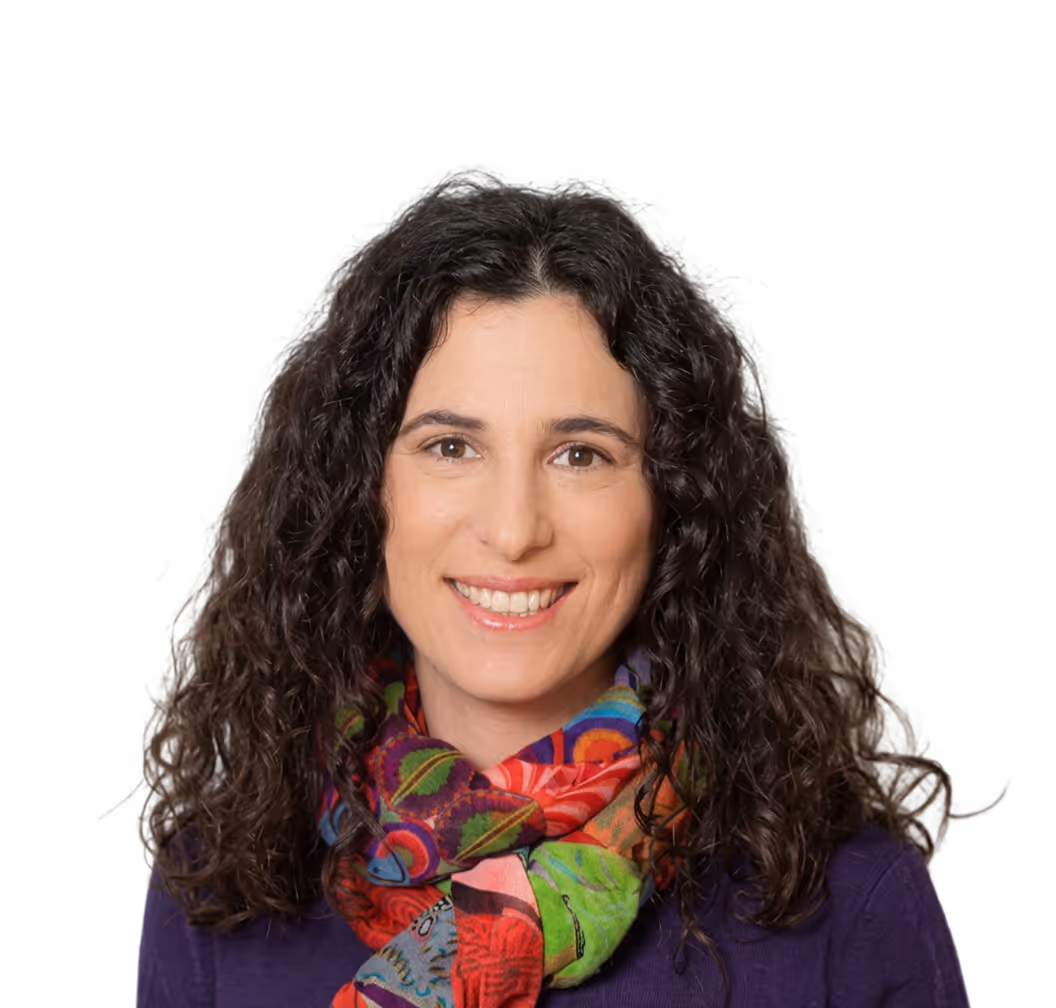Smiling woman with curly dark hair wearing a colorful scarf and purple top against a plain background.