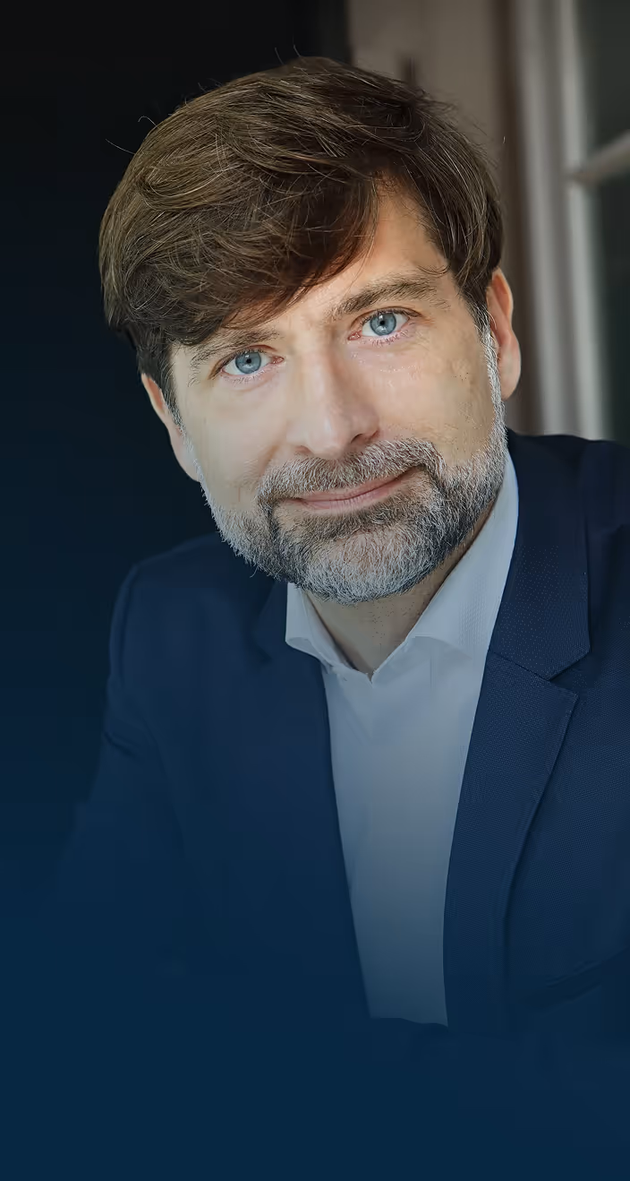 Portrait of Istvan Petak, with blue eyes, beard, and brown hair wearing a navy suit and white shirt.
