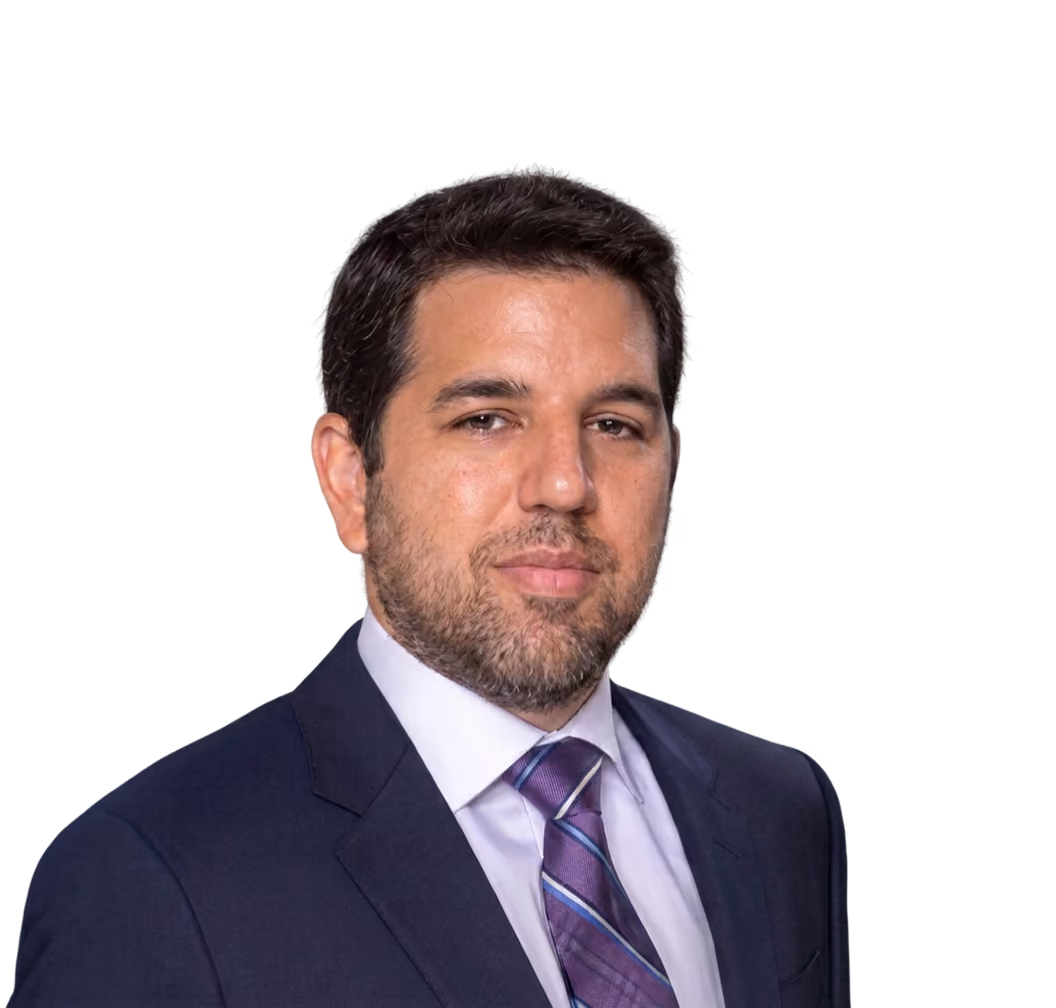 Man with dark hair and beard wearing a dark suit, white shirt, and purple striped tie.
