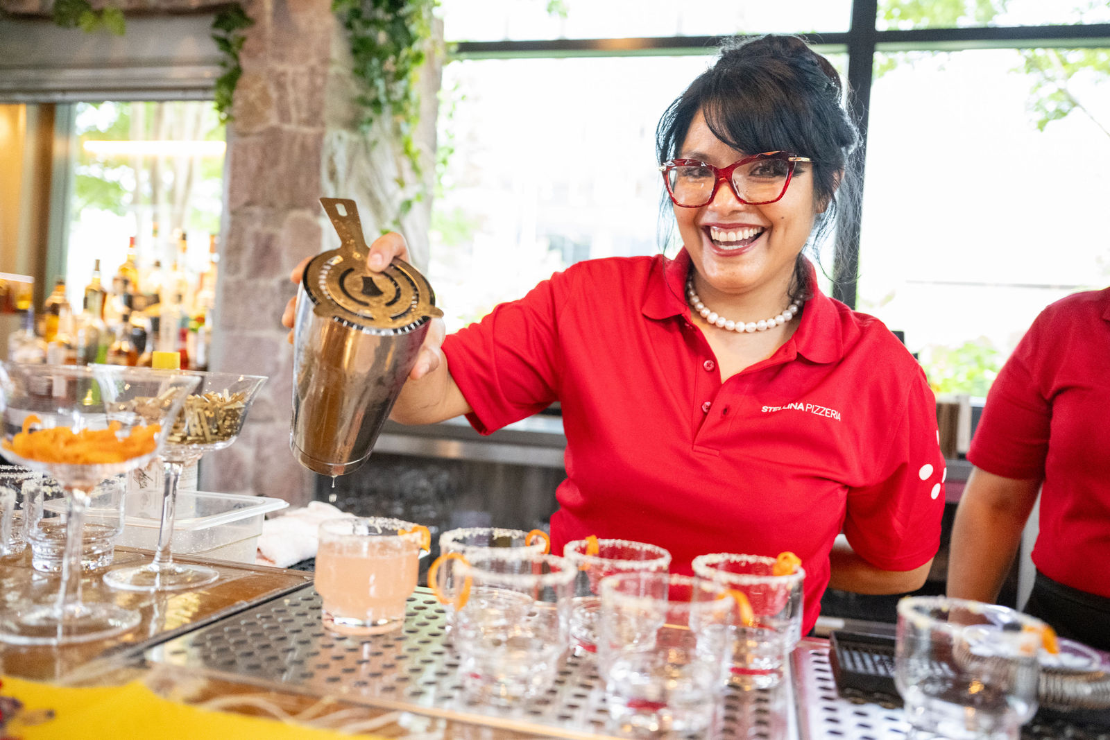 Claudia, bartender at Stellina Pizzeria, shaking a cocktail and smiling behind the bar at Capital One Center Culinary Week 2026