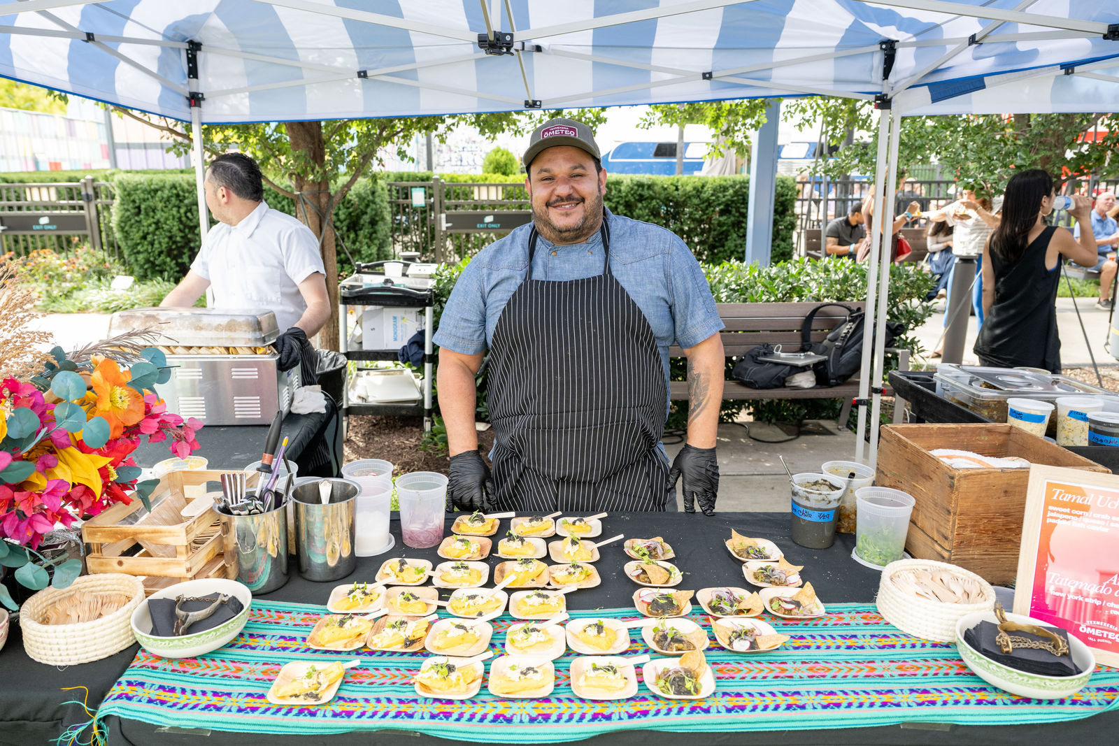 Chef smiling behind a display of tasting dishes at an outdoor event booth at Capital One Center Culinary Week 2026