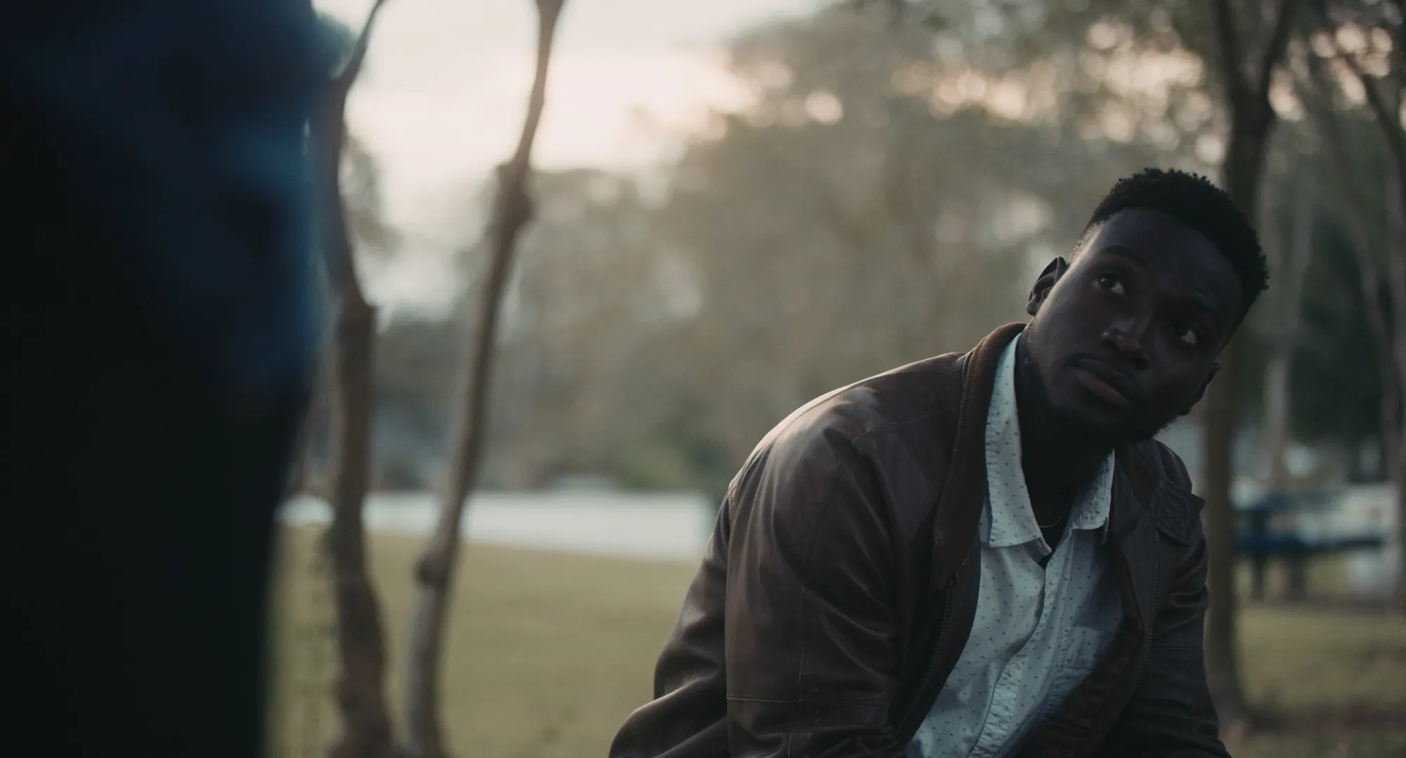 17 Year Locust film still showing the young Haitian man Renee sitting in a park, looking up at someone out of frame