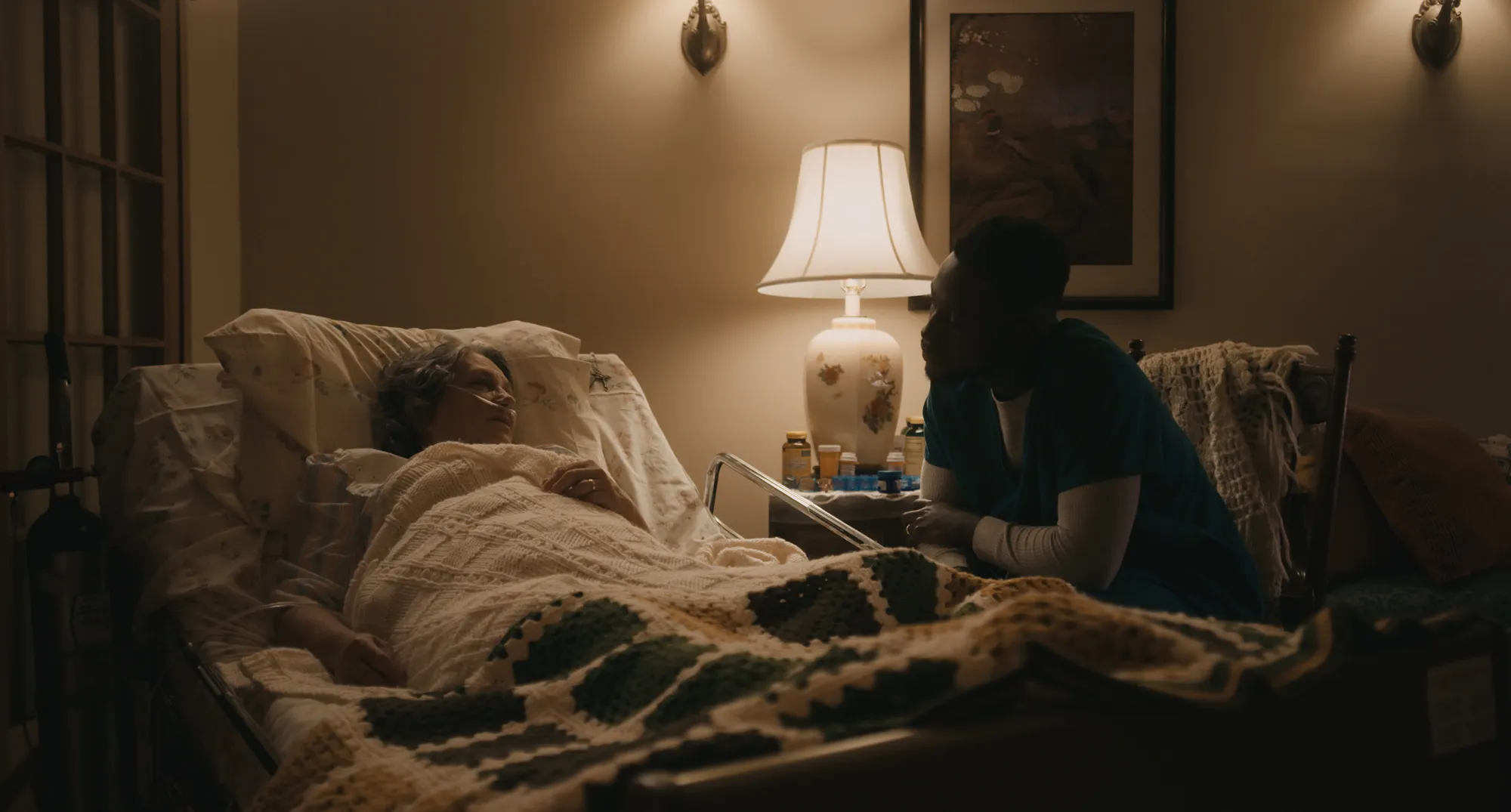17 year locust film still showing an older sickly woman from Louisiana in bed visiting with a young Haitian man sitting in a chair beside her. 