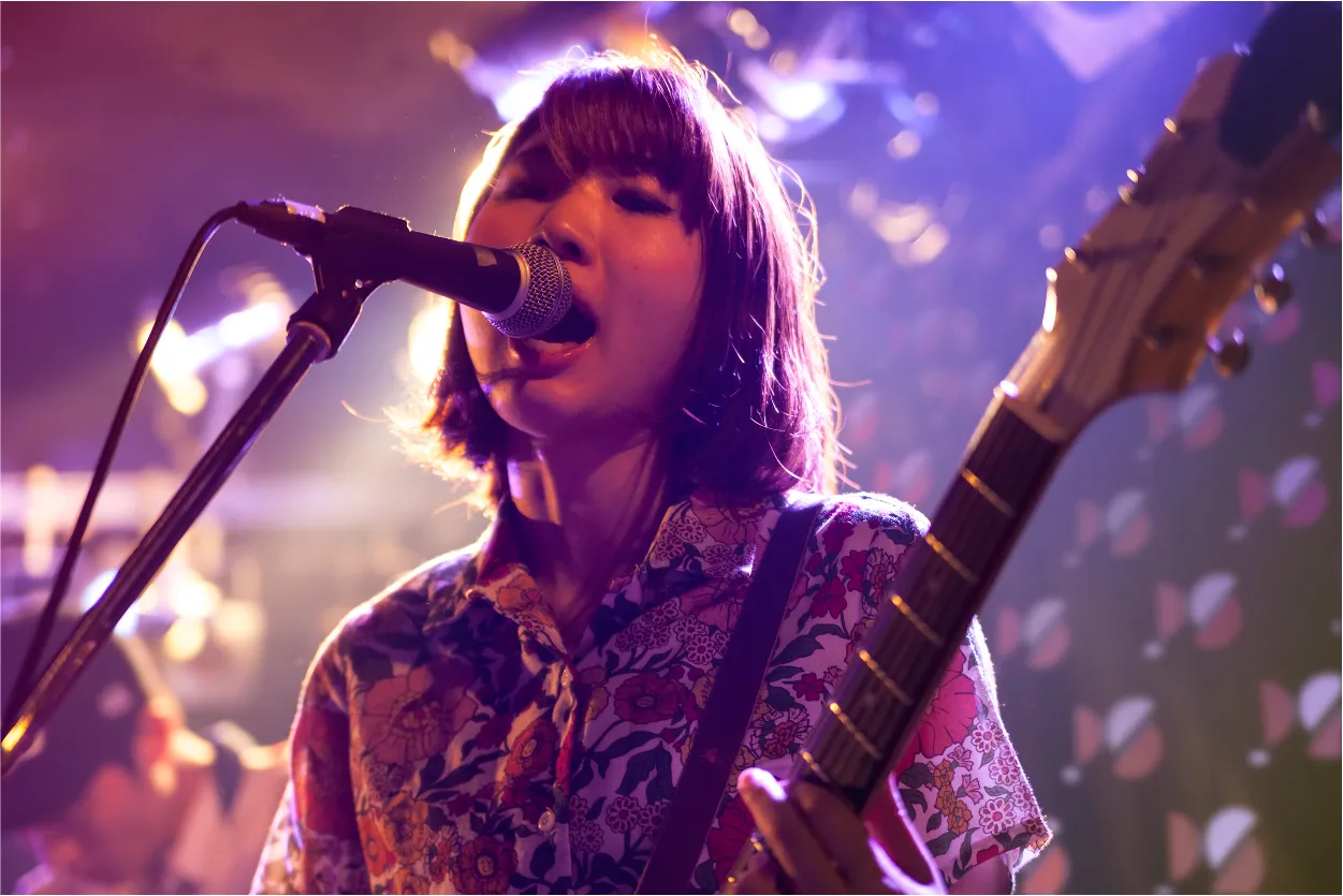 pronounced sound guitar player with logo wall shown behind her