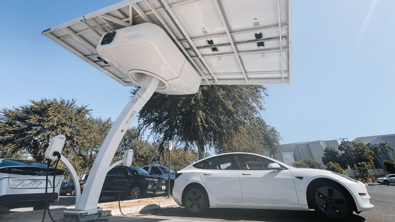 White Tesla Model 3 parked and charging under a solar carport with an integrated EV charging pole.