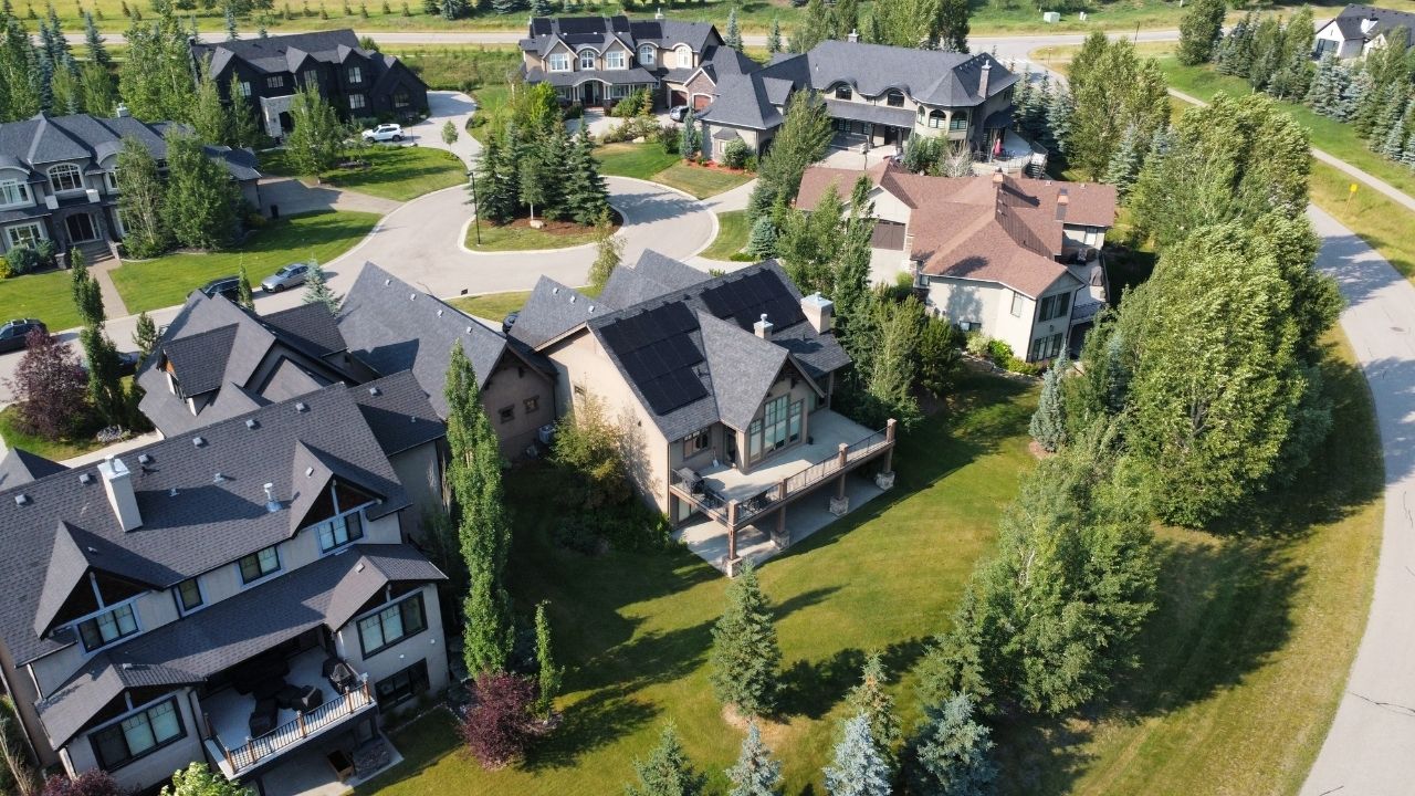 Aerial view of a residential solar panel installation on a luxury home in Calgary, Alberta, featuring black rooftop solar panels in a tree-lined suburban neighbourhood.