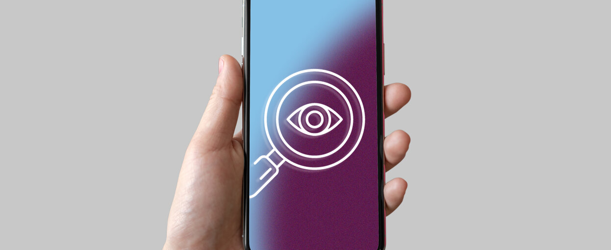 A hand holding a phone showing a magnifying glass over an eye