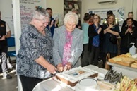 Colunteer Andrea and consumer Brenda cut a cake to celebrate the merger of CTST and MCCA