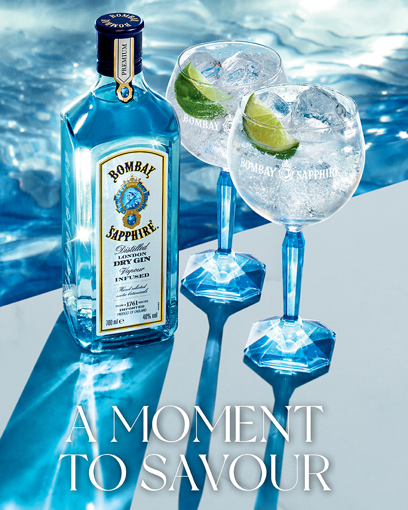 Bottle of Bombay Sapphire besides a glass and a Schweppes can on top of a marble table