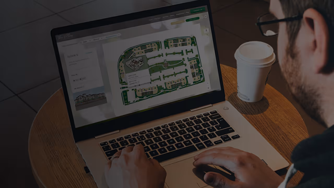 Man in a coffee shop looking at a website on his laptop with a map of an apartment complex.