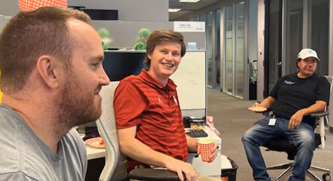Three ResMan team members sitting around their desks chatting and drinking coffee