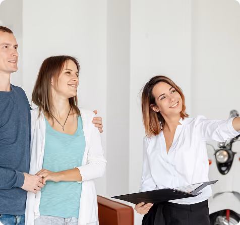 Real estate agent showing a smiling couple around a home interior while holding a folder.