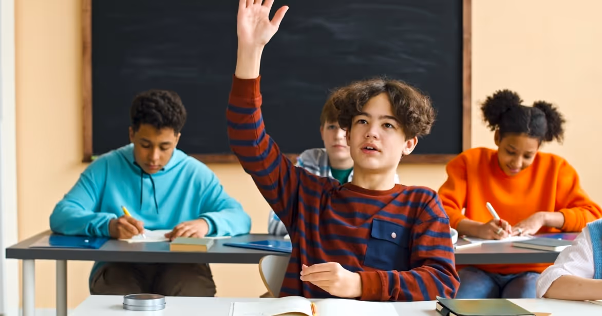 Child raising hand in classroom – symbolising helping children thrive in foster care