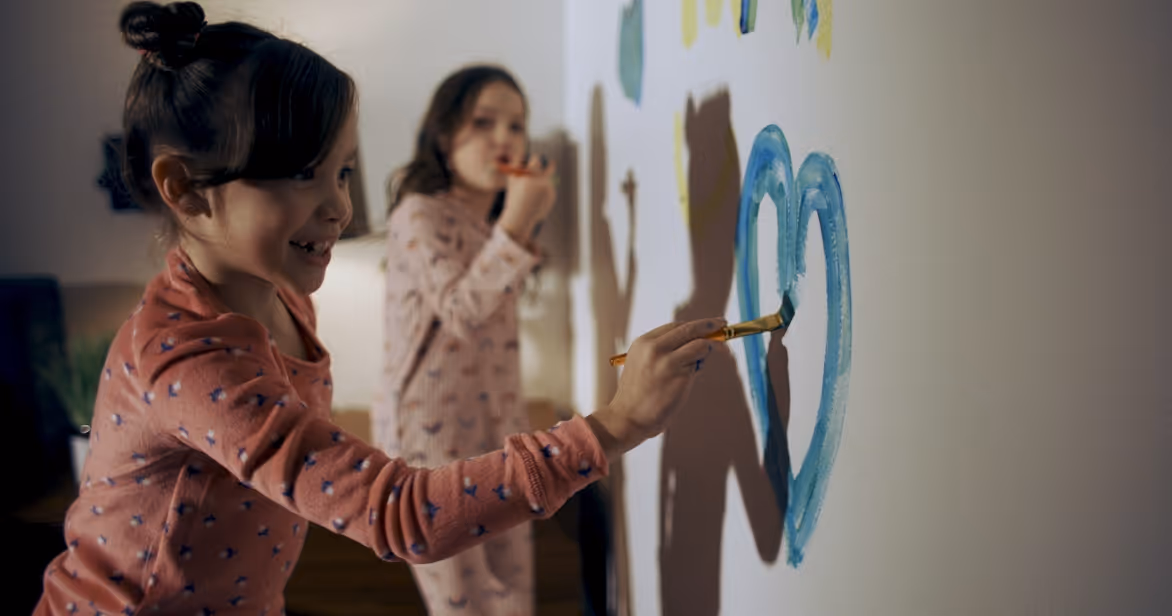Two young girls in pyjamas painting hearts on a wall – representing joy and creativity in a foster care home.