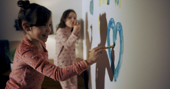 Two young girls in pyjamas painting hearts on a wall – representing joy and creativity in a foster care home.
